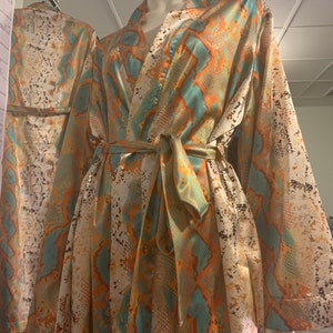 May include: A long-sleeved robe with a snakeskin print in shades of orange, teal, and brown. The robe has a tie belt and a V-neck.