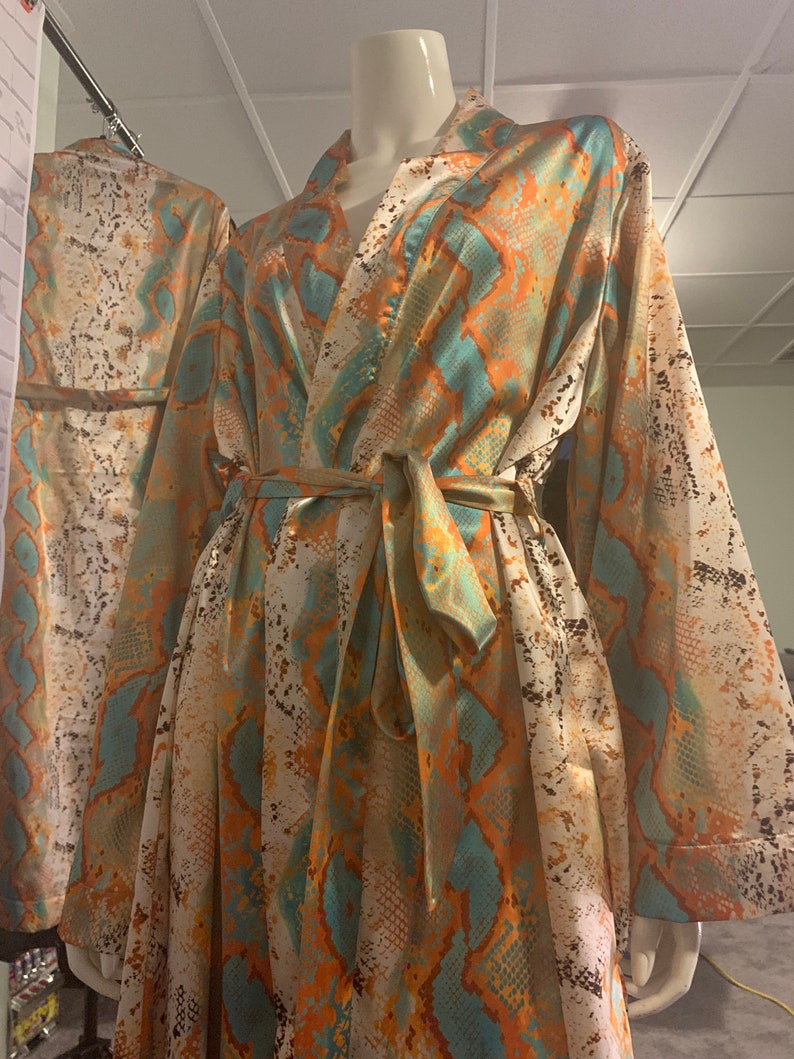 May include: A long-sleeved robe with a snakeskin print in shades of orange, teal, and brown. The robe has a tie belt and a V-neck.