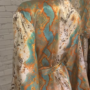 May include: A white, orange, and teal satin robe with a snake skin pattern. The robe has a tie belt and long sleeves.