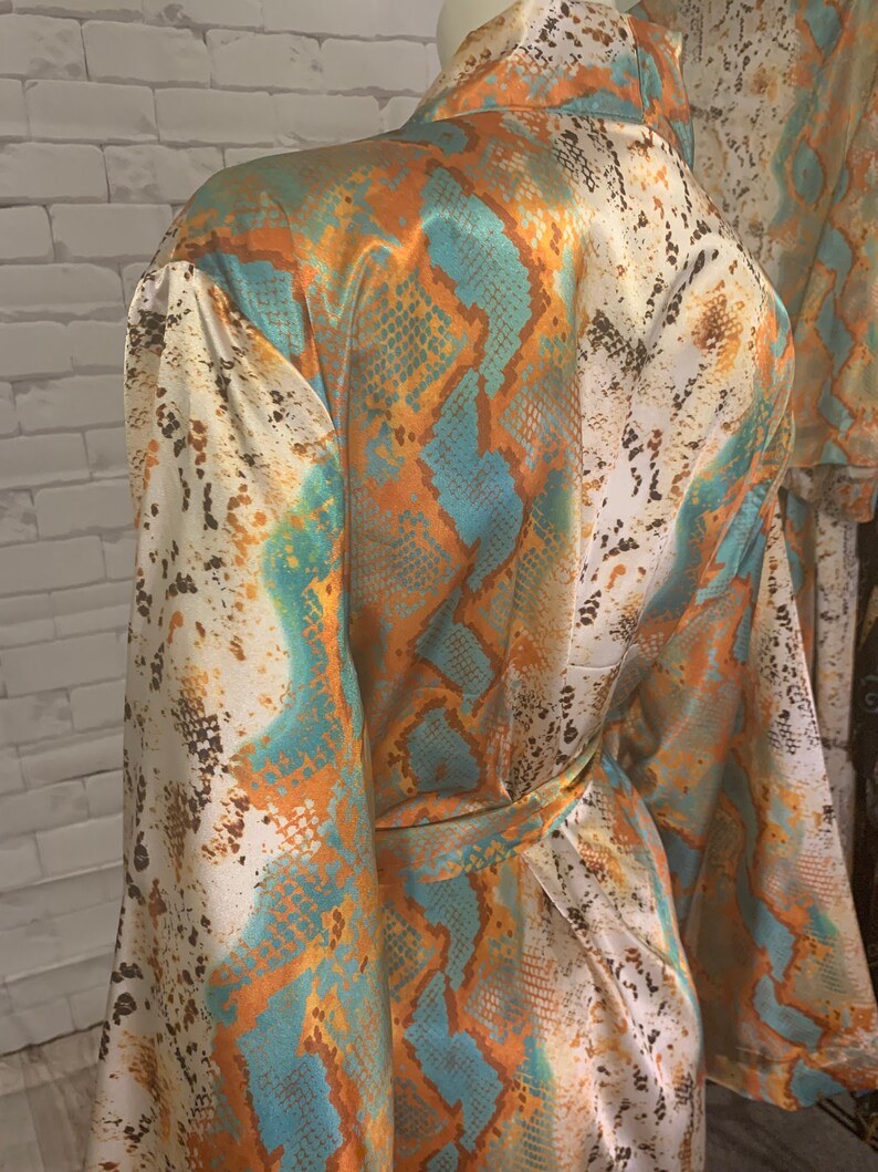 May include: A white, orange, and teal satin robe with a snake skin pattern. The robe has a tie belt and long sleeves.