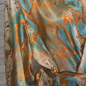 May include: A long-sleeved robe with a snakeskin print in shades of orange, teal, and white. The robe has a tie belt and a relaxed fit.