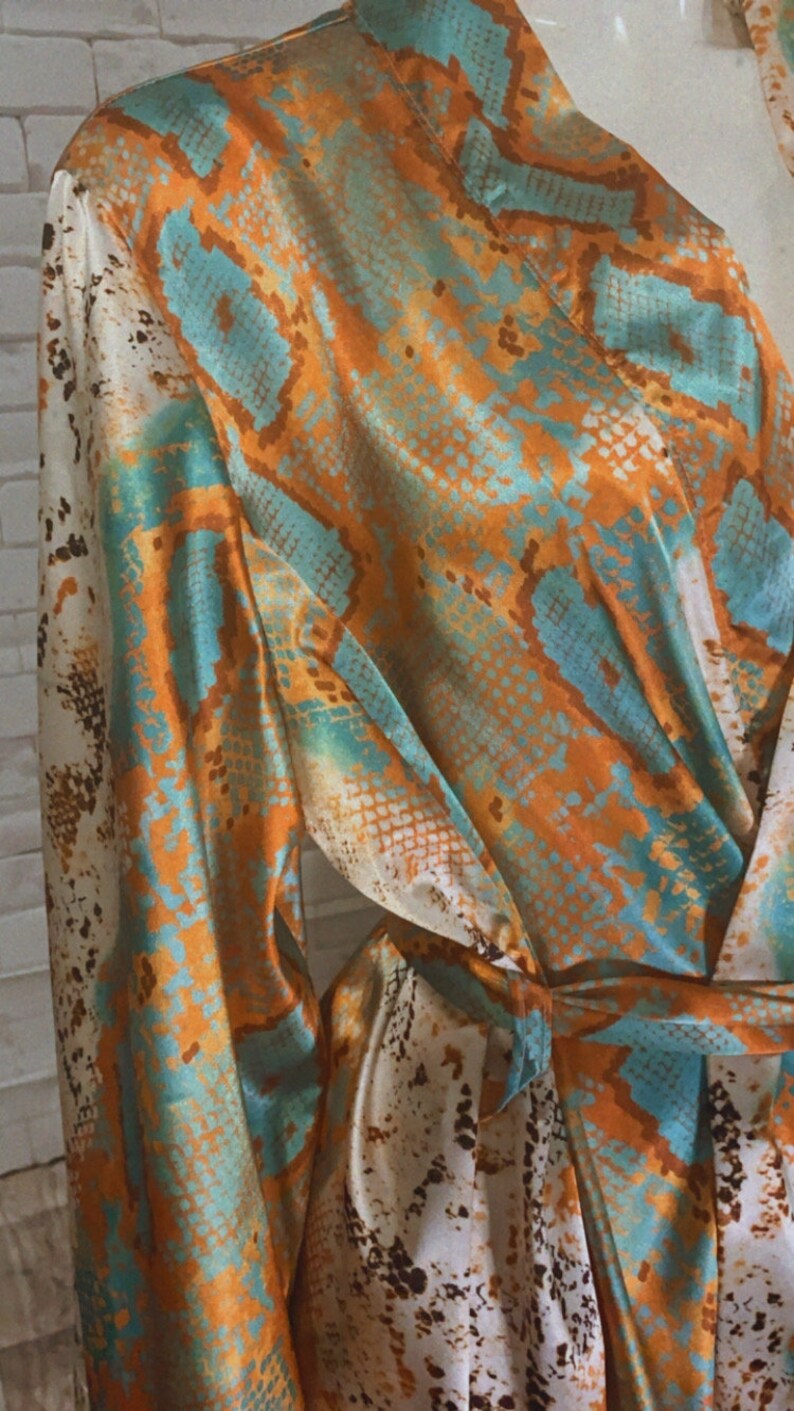 May include: A long-sleeved robe with a snakeskin print in shades of orange, teal, and white. The robe has a tie belt and a relaxed fit.