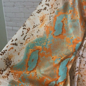 May include: A white, orange, and teal snakeskin patterned fabric. The fabric has a silky texture.