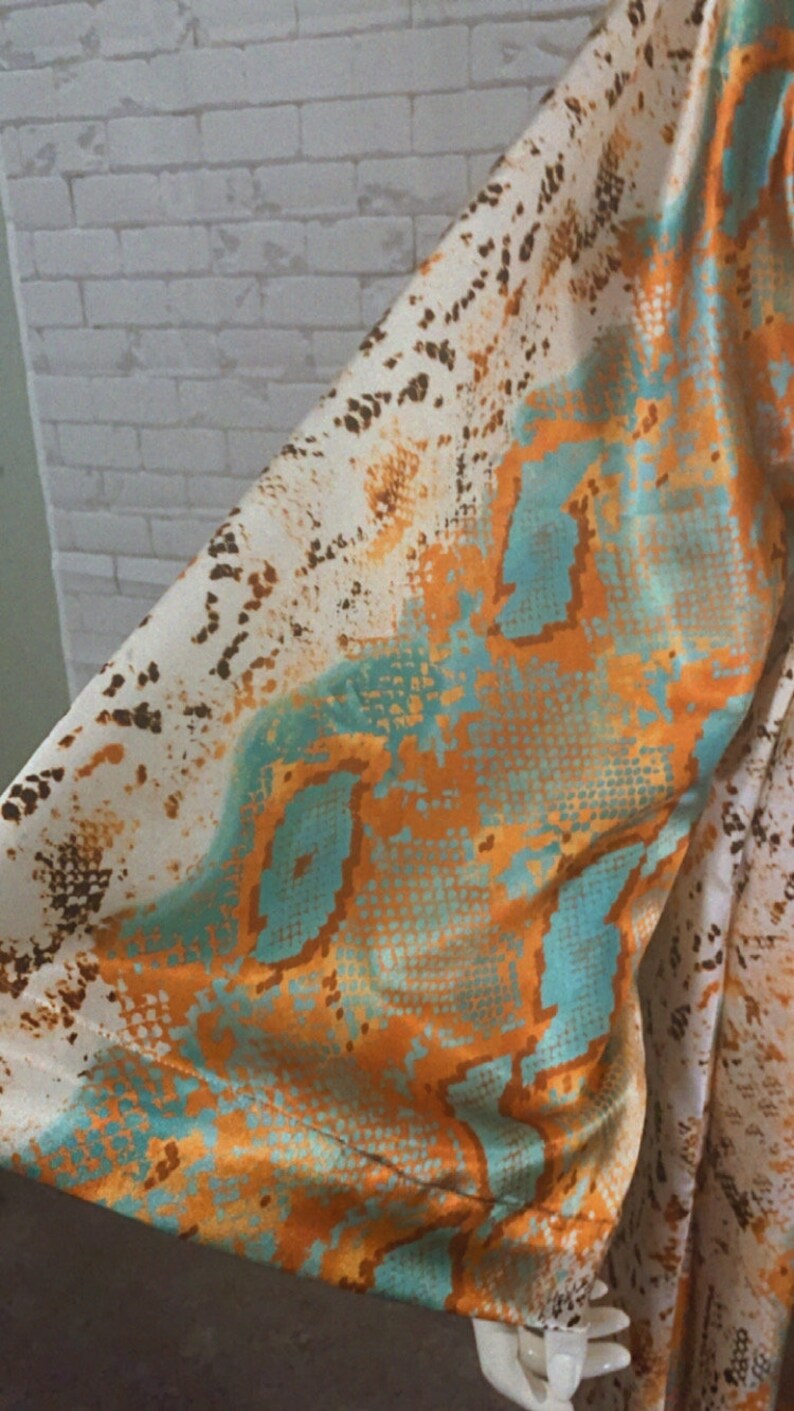 May include: A white, orange, and teal snakeskin patterned fabric. The fabric has a silky texture.