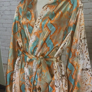May include: A long-sleeved robe with a snakeskin print in shades of orange, teal, and white. The robe has a tie belt and a V-neck.