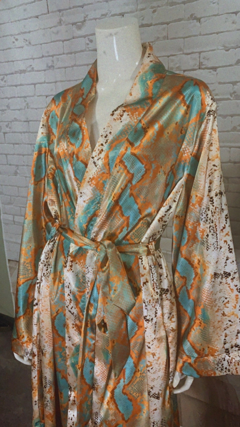 May include: A long-sleeved robe with a snakeskin print in shades of orange, teal, and white. The robe has a tie belt and a V-neck.