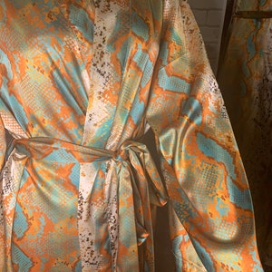 May include: A long-sleeved robe with a snakeskin pattern in shades of orange, blue, and white. The robe has a tie belt and a V-neck.