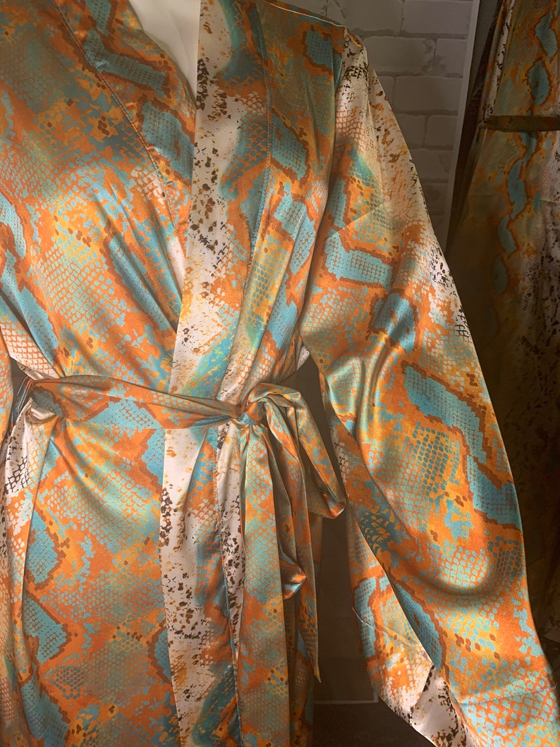 May include: A long-sleeved robe with a snakeskin pattern in shades of orange, blue, and white. The robe has a tie belt and a V-neck.