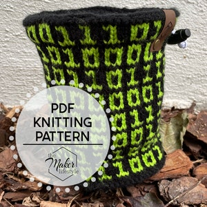 May include: A black and green knitted pouch with a leather strap and a black pen. The pouch is sitting on a bed of brown wood chips. The text "PDF Knitting Pattern the Maker Lifestyle" is on a white circle.