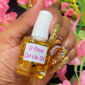 May include: A clear glass bottle with a white cap and a pink label that reads "D Flora Cuticle Oil".