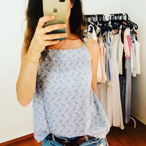 May include: A blue and white paisley print sleeveless top with a square neckline. The top is loose fitting and has a relaxed silhouette.