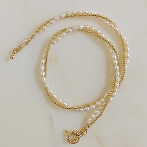 Puede incluir: Un delicado collar de oro y perlas blancas con un cierre de oro. El collar está hecho de pequeñas perlas redondas y cuentas doradas.