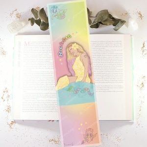 May include: A colorful bookmark with a mermaid illustration and the text "Bichota" in pink letters. The bookmark features a rainbow gradient background and stars.
