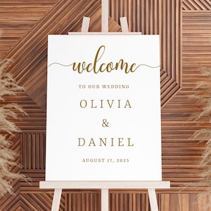 Puede incluir: Un cartel de bienvenida blanco con letras doradas. El cartel dice "Bienvenido a nuestra boda Olivia & Daniel 17 de agosto de 2025".