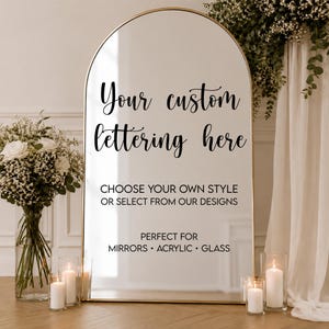 May include: An arched mirror with a thin gold frame featuring black text that reads: Your custom lettering here, CHOOSE YOUR OWN STYLE OR SELECT FROM OUR DESIGNS, PERFECT FOR MIRRORS • ACRYLIC • GLASS. The mirror is reflective and stands upright.