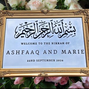 Pu&ograve; includere: Un cartello con cornice dorata con un'iscrizione araba, "بسم الله الرحمن الرحيم", e il testo "Benvenuti al Nikkah di Ashfaaq e Marie 22 settembre 2026".