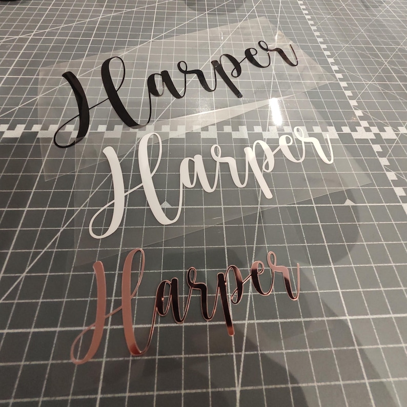 May include: Three vinyl decals with the name "Harper" written in different styles. The top decal is black, the middle decal is white, and the bottom decal is rose gold.