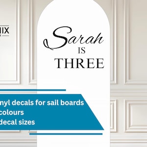 May include: A white backdrop displays a black logo for "The Phoenix Emporium" and the text "Sarah IS THREE". Beneath, a teal banner promotes custom vinyl decals for sail boards, offered in various colours and sizes.