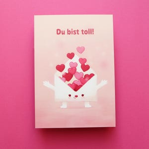 Könnte beinhalten: Eine Grußkarte mit rosa Hintergrund zeigt einen Cartoon-Umschlag-Charakter mit Armen und Beinen, der rote und rosa Herzen verschüttet. Der Text "Du bist toll!" ist oben in Rot geschrieben.