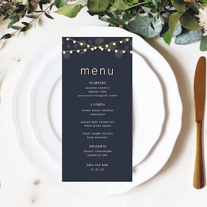 May include: A dark blue menu card with a gold border and white text. The menu features a list of starters, entrees, and desserts. The top of the card has a string of lights with a white glow. The text at the bottom of the card reads "John and Kim 01.01.22".