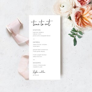 May include: A white wedding menu with black text. The menu is titled "time to eat" and lists the starters, entrees, and desserts for the wedding reception. The bottom of the menu includes the names "stephen and kim" and the date "01.25.22".