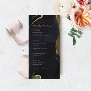 May include: A black and gold wedding menu with a marble-like background. The menu lists appetizers, entrees, and desserts. The text at the bottom reads "Stephen and Kim 01.25.22".