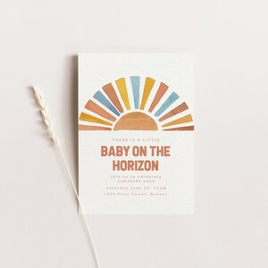 May include: A baby shower invitation with a watercolor illustration of a sunset in shades of orange, yellow, blue, and brown. The text reads "There is a little baby on the horizon. Join us to celebrate Samantha Anne. Saturday June 15, 11am. 1234 First Street, Denver."