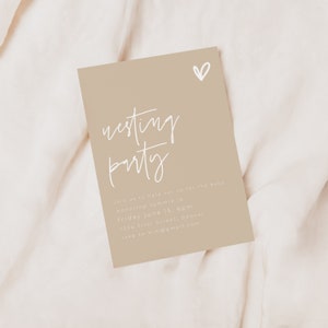 May include: A beige card with white text that reads "nesting party" and includes details for a baby shower. The card also has a small white heart in the top right corner.