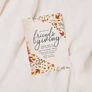 Pu&ograve; includere: Un biglietto d'invito Friendsgiving con sfondo crema e illustrazioni di foglie e zucche autunnali. Il biglietto presenta il testo "Join us for Friendsgiving" in elegante scrittura, insieme ai dettagli dell'evento.