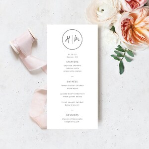 May include: A white menu with a black circle containing the initials "HM" and the date "01.25.22" followed by the text "Denver, CO". The menu lists starters, entrees, and desserts.