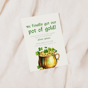 May include: A white invitation card with green text that reads "we finally got our pot of gold!"  Join us for a sip to see to meet our little leprechaun Oliver James. Friday March 15 at 5pm 1234 First Street Denver, CO. The card features a watercolor illustration of a gold pot filled with gold coins and green shamrocks.