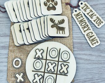 May include: A wooden tic-tac-toe board with X and O pieces, a set of square memory game tiles featuring animal and paw print engravings, and two wooden tags labeled TIC TAC TOE and MEMORY GAME, all stored in a tan burlap drawstring bag.