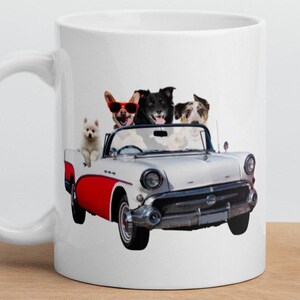 May include: White ceramic mug with a graphic of four dogs riding in a white convertible car with red accents. The dogs are wearing sunglasses and are smiling.