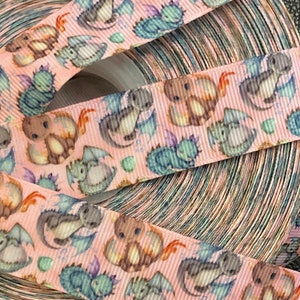 May include: Pink ribbon with a repeating pattern of cartoon dragons. The dragons are in various shades of blue, brown, and pink.