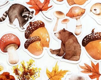 May include: A set of autumn-themed stickers featuring a raccoon, a bear, a rabbit, mushrooms, acorns, and leaves. The stickers are illustrated in a watercolor style with brown, orange, red, and yellow colors.