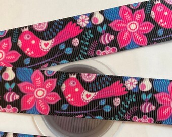 Può includere: Un rotolo di nastro nero con una stampa floreale e di uccelli colorata. Il nastro presenta fiori rosa, foglie blu e uccelli rosa con accenti bianchi.