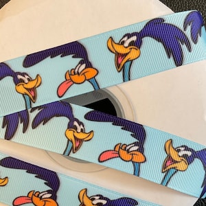 May include: Blue and light blue ribbon with a repeating pattern of cartoon roadrunner characters. The roadrunner is a cartoon character known for its speed and ability to outsmart Wile E. Coyote.