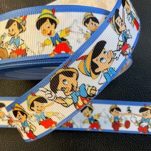 May include: White and blue ribbon with a repeating pattern of Pinocchio characters. The ribbon is rolled up and the characters are in various poses.