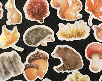 May include: A set of 20 watercolor stickers featuring woodland animals, plants, and mushrooms. The stickers are on a black background and include a fox, a squirrel, a hedgehog, a deer, a bear, a raccoon, a rabbit, and various trees and mushrooms.
