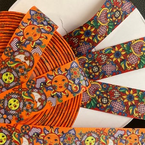 Puede incluir: Cinta naranja con un patrón colorido de sol y flores. La cinta está enrollada alrededor de un carrete.