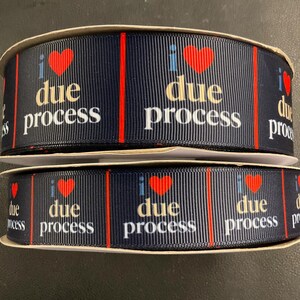 May include: Two spools of navy blue ribbon with the text "I due process" in white and red. The ribbon has a vertical red stripe design and a red heart graphic. The ribbon is likely used for crafting or decoration.