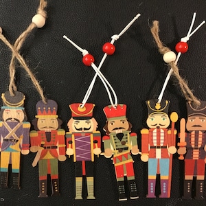 以下が含まれることがあります： カラフルなディテールと異なるデザインの、木製のナッツクラッカーオーナメント6個。各オーナメントには、吊り下げ用の紐が付いています。