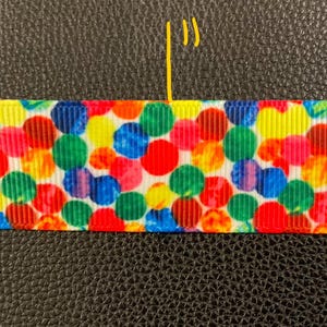 May include: A white ribbon with a colorful confetti pattern. The confetti is in various shades of red, yellow, blue, green, and orange.