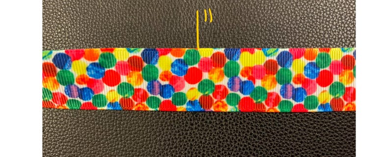 May include: A white ribbon with a colorful confetti pattern. The confetti is in various shades of red, yellow, blue, green, and orange.