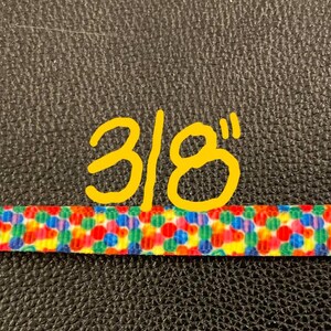 May include: A close-up of a colorful ribbon with a 3/8 inch width. The ribbon is made of a white fabric with a pattern of small, colorful circles.