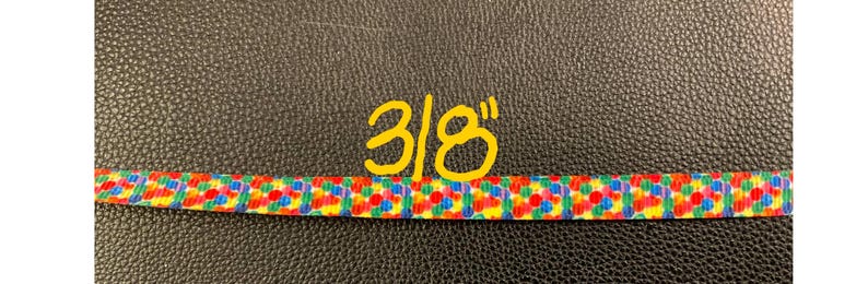 May include: A close-up of a colorful ribbon with a 3/8 inch width. The ribbon is made of a white fabric with a pattern of small, colorful circles.