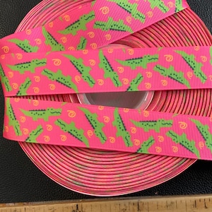 May include: Pink and green ribbon with a repeating pattern of alligators. The ribbon is rolled up and the pattern is visible on multiple layers.