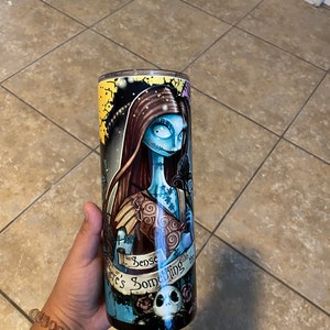 May include: A black and blue stainless steel tumbler featuring a graphic of Sally from The Nightmare Before Christmas. The tumbler has a white and gold rim and the text "There's Something About You" in a banner.