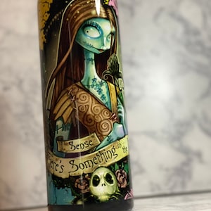 May include: A black and green stainless steel tumbler featuring a graphic of Sally from The Nightmare Before Christmas. The tumbler has the text "I sense something in the air" on it.