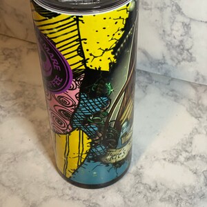 May include: A stainless steel tumbler featuring a colourful graphic of a character from the Nightmare Before Christmas film. The graphic has a patchwork design with yellow, blue, pink and green colours. The text "There's" is visible on the tumbler.